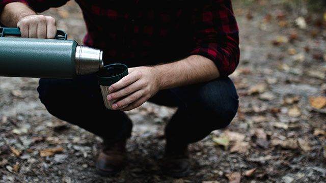 man crouching down holding a thermos