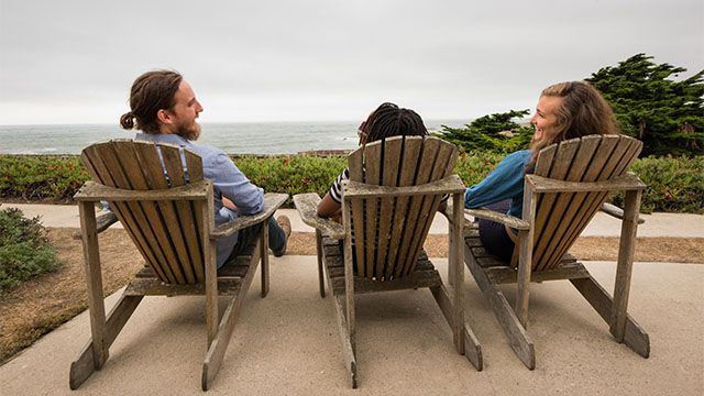 Three people on chairs looking at the view of the Pacific Ocean
